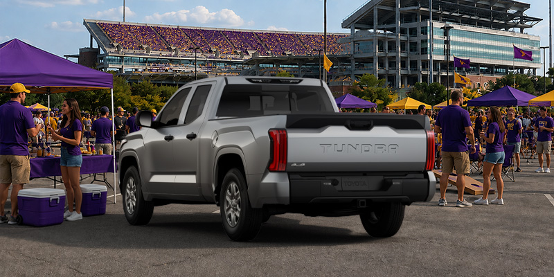 A Toyota Tundra features a silver exterior finish and a bold tailgate design parked outside a stadium.